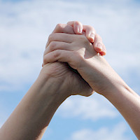Kahden henkilön kädet yhdessä, taustalla taivas