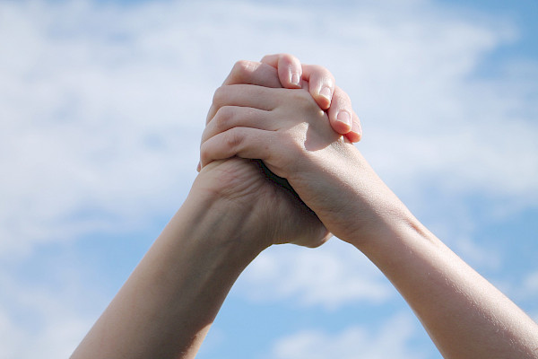 Kahden henkilön kädet yhdessä, taustalla taivas