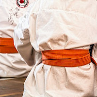 Kaksi karatepuvuissa lattialla istuvaa lasta ja heillä oranssit vyöt