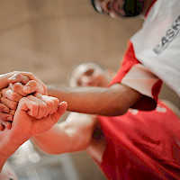 Koripallojoukkueen pelaajilla kädet päällekkäin ennen kannustushuutoa