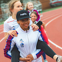 Lapset kantavat toisiaan reppuselässä yleisurheilukentällä