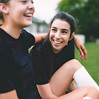 Tytöt istuvat jalkapallokentällä ja hymyilevät