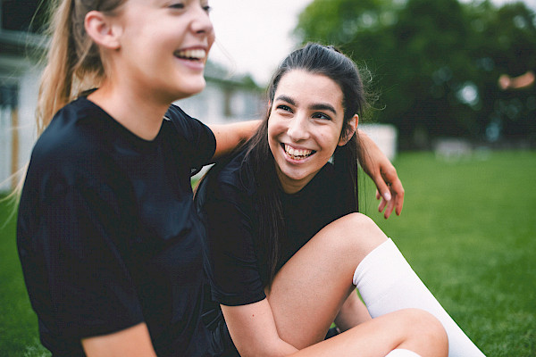 Tytöt istuvat jalkapallokentällä ja hymyilevät