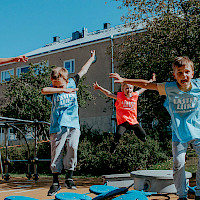 Lapset hyppäävät ilmaan leikkikentällä Lasten liike -paidat yllään