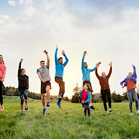 Ryhmä eri-ikäisiä liikkujia hyppää ilmaan auringonlaskussa