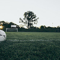Jalkapallokenttä, maali ja pallo auringonlaskussa