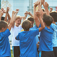 Lapset iloitsevat urheilukentällä, hymyilevät ja pitävät käsiään ylhäällä