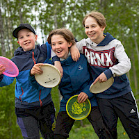 Kolme iloista nuorta frisbeet kädessä frisbeegolf-radalla