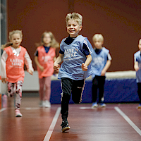 Lapset juoksevat juoksuradalla Lasten Liike -liivit päällään