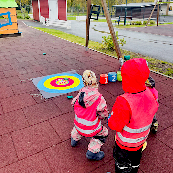Kolme pientä lasta heittää hernepusseja Jekku-jänö-heittoalustaan.